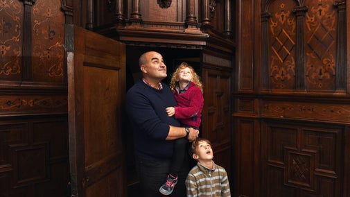 Father holding a toddler, with a small boy standing next to him. They are looking upwards at the elaborate wooden carvings in the house at Sizergh.